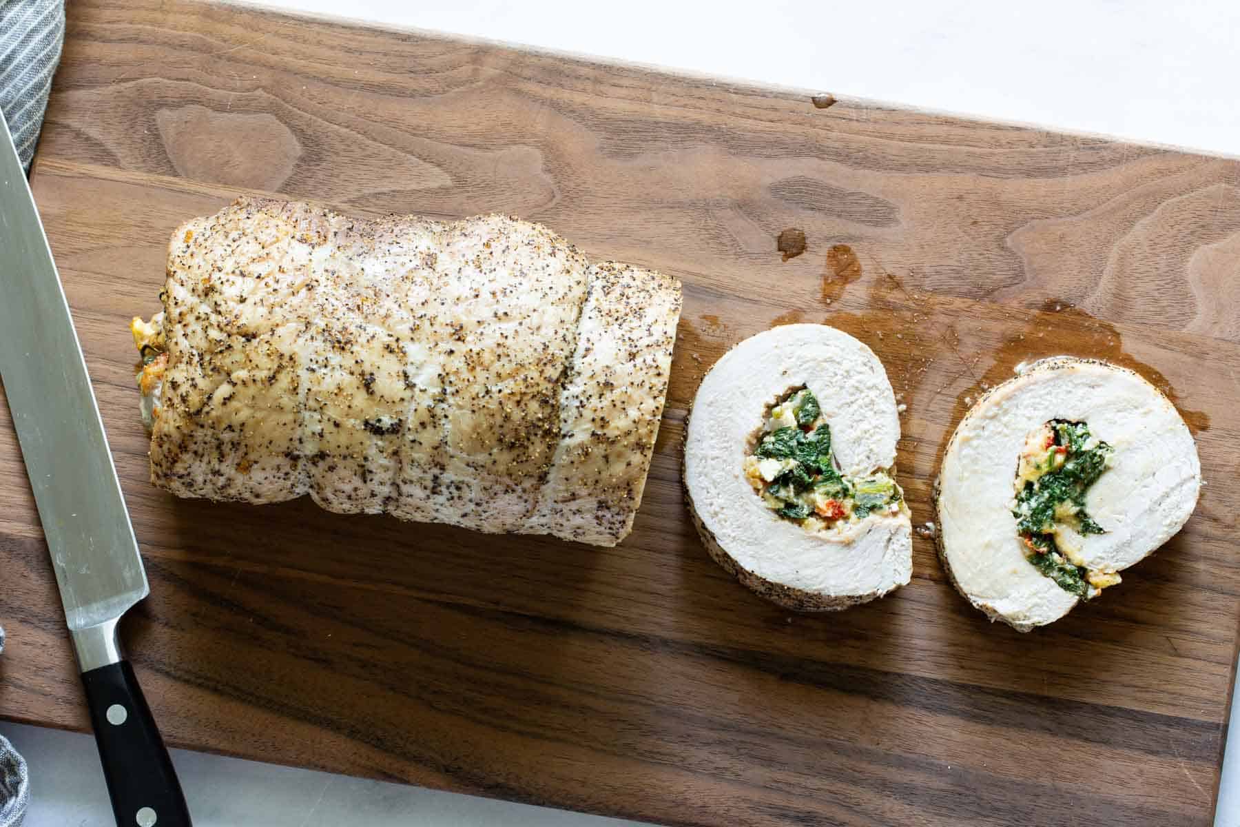 A sliced stuffed pork loin on a cutting board.