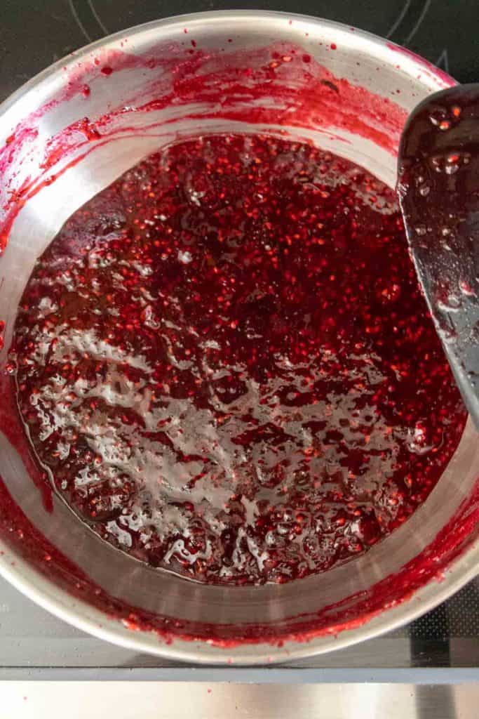 Close-up of a pot filled with simmering blackberry jam being stirred with a spoon.