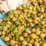 A plate of seasoned chickpeas mixed with chopped vegetables, served with a piece of naan bread.