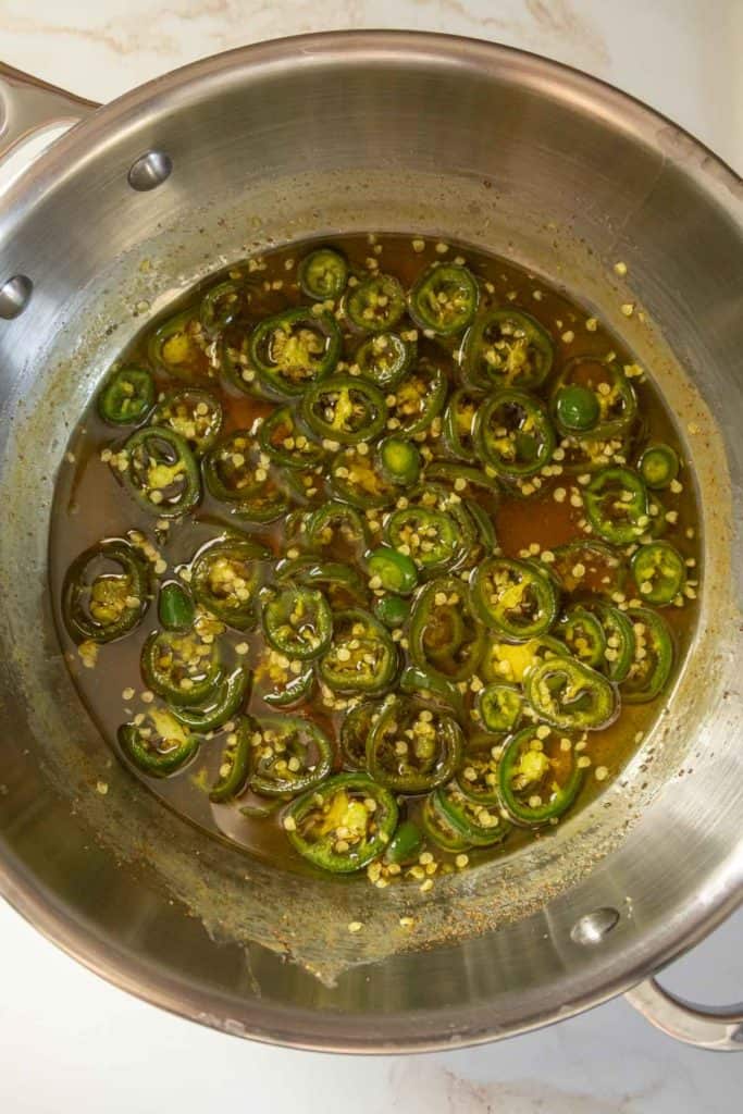 A stainless steel pot containing sliced jalapeños and seeds in a liquid mixture.