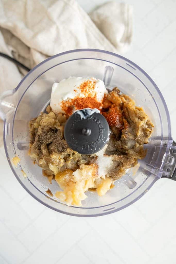 A food processor bowl containing mashed vegetables, yogurt, and various spices ready to be blended.