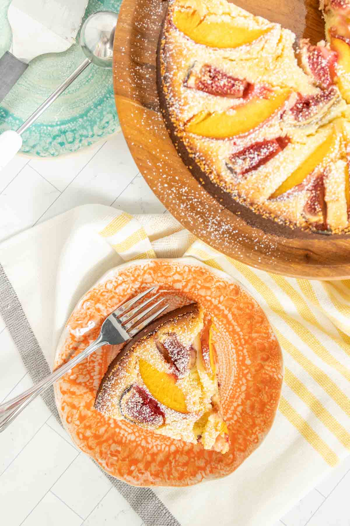 A slice of fig and nectarine cake on an orange plate next to a fork, with the rest of the tart on a wooden serving board in the background.