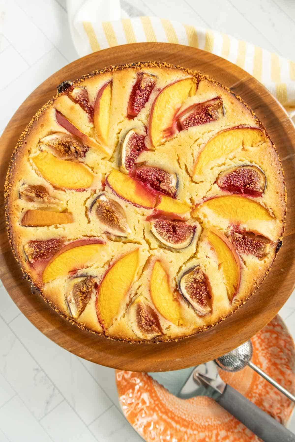 Top view of a round, freshly baked fruit cake with sliced nectarines and figs arranged in a circular pattern on a wooden serving platter.