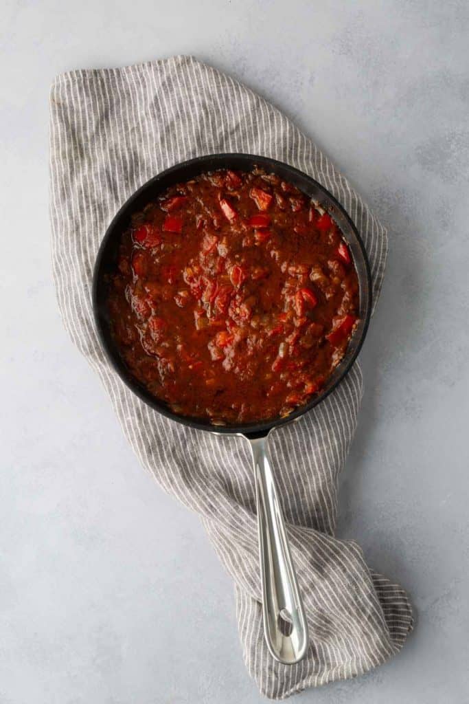 A skillet filled with a meat and tomato sauce mixture, placed on a striped cloth on a light gray surface.