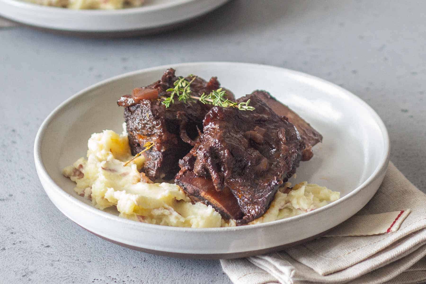 A plate with braised short ribs garnished with herbs, served over mashed potatoes.