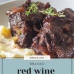 A plate of braised red wine short ribs served with mashed potatoes, garnished with fresh thyme.