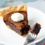 A slice of chocolate chess pie topped with whipped cream on a white plate, with a bite taken out by a fork, against a light blue background. Text overlay reads: "chocolate CHESS PIE".