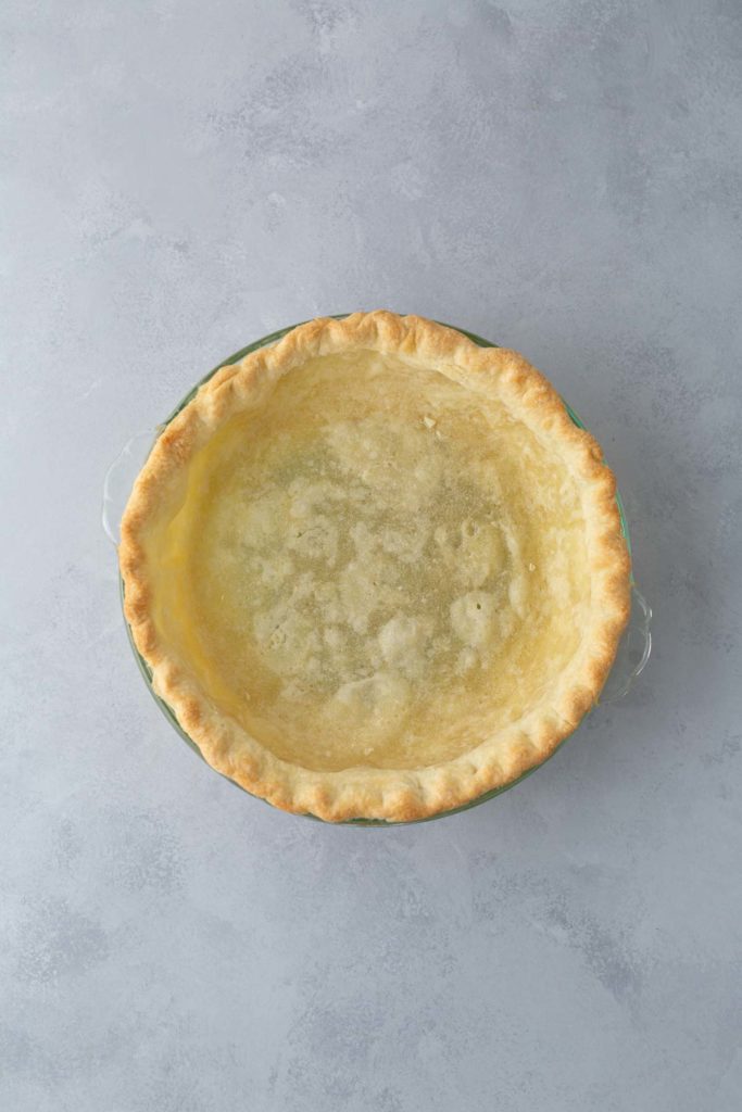 A baked empty pie crust in a pie dish is placed on a light gray surface.