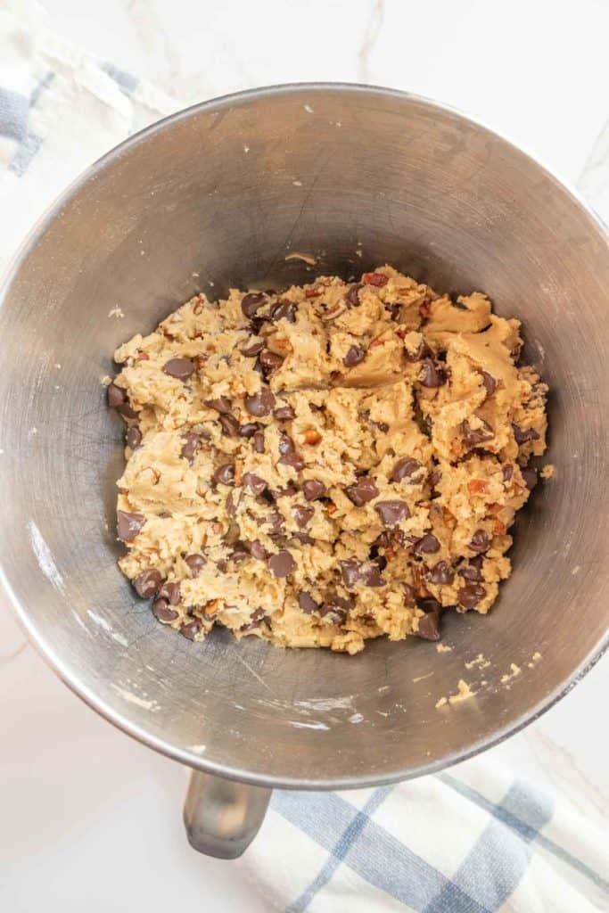 A mixing bowl filled with raw cookie dough containing chocolate chips and nuts.