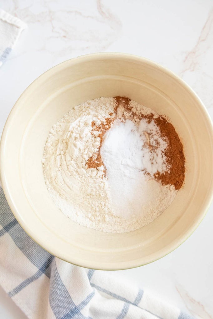 A mixing bowl with flour, baking powder, and a brown spice on a light-colored cloth.