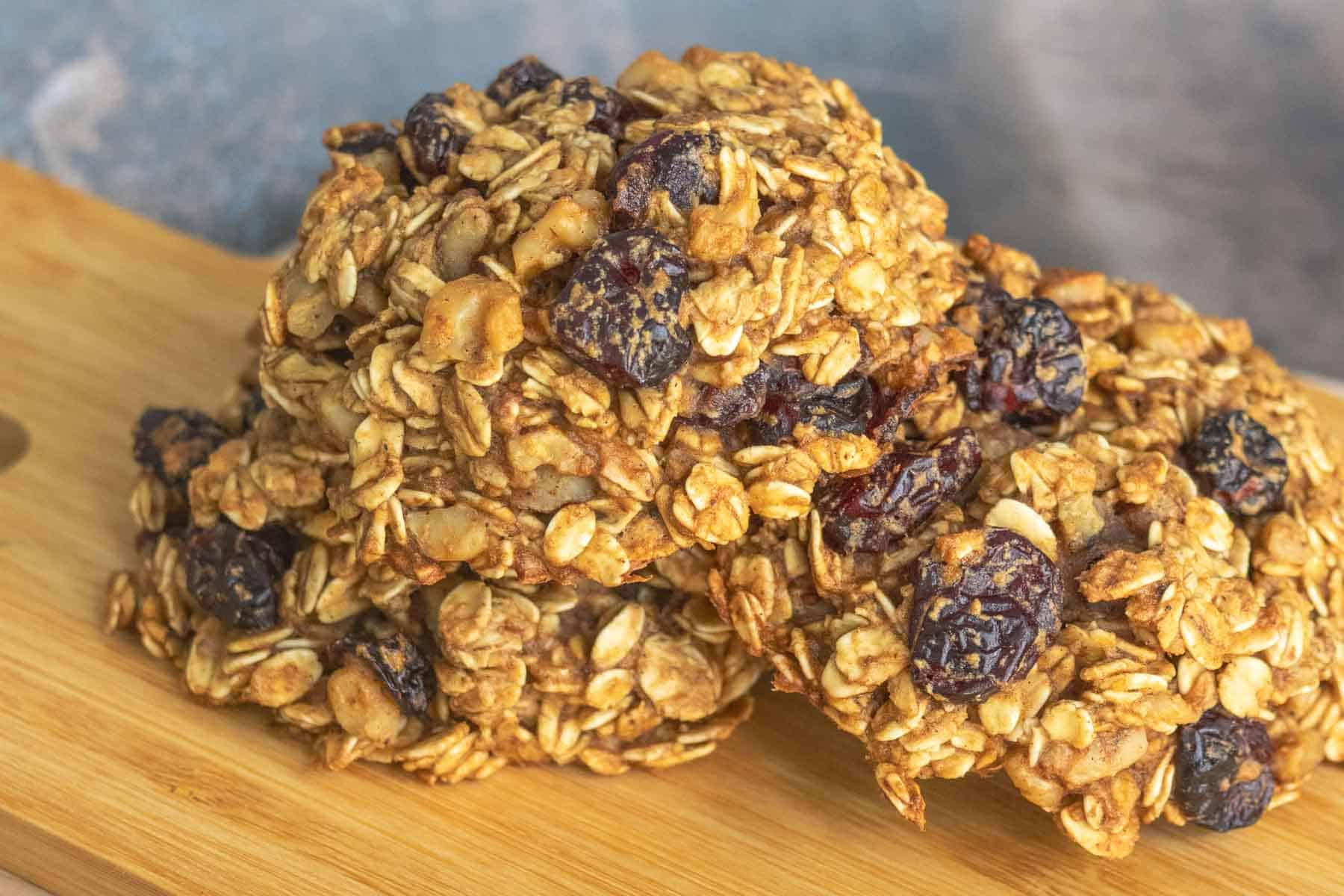 A stack of homemade oatmeal cookies with dried berries and oats sits on a wooden surface.