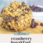 A close-up of a cranberry breakfast cookie with a bowl of dried cranberries in the background. Text on the image reads "cranberry breakfast cookies - sweet & satisfying.