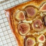 Rectangular fig tart with a golden-brown crust on a cooling rack. The tart is topped with figs and appears freshly baked.