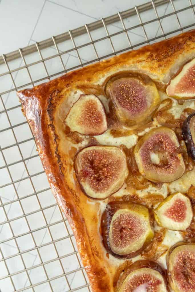 Rectangular fig tart with a golden-brown crust on a cooling rack. The tart is topped with figs and appears freshly baked.