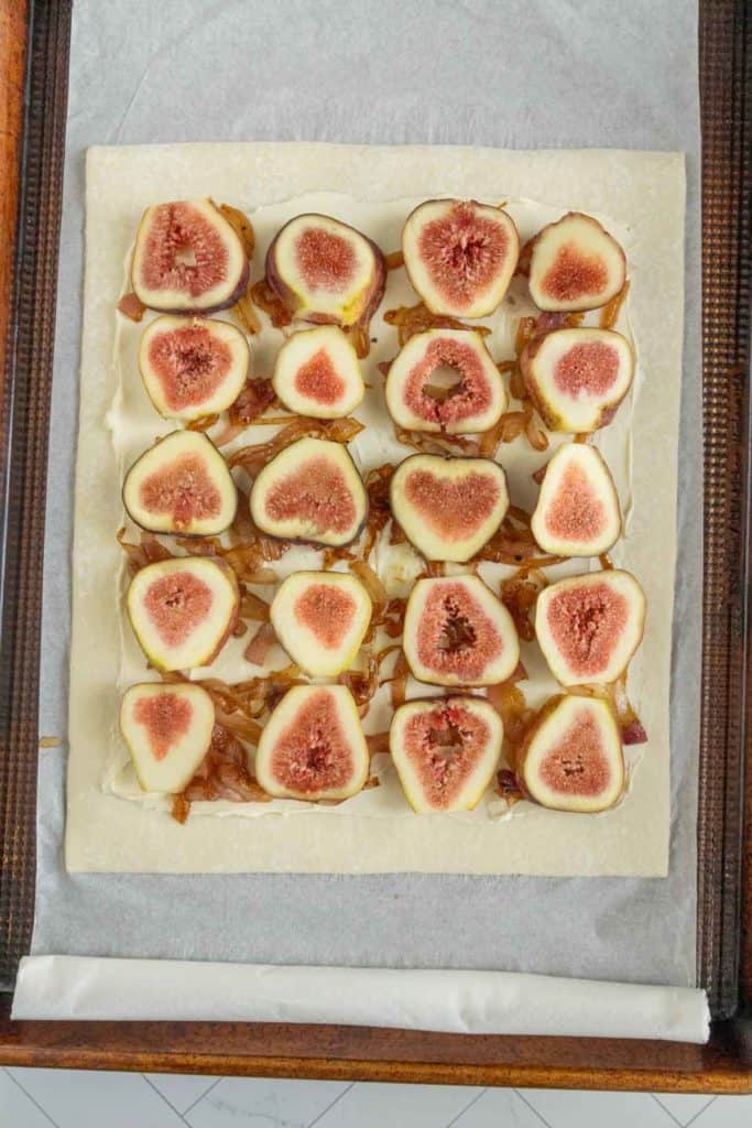 A rectangular pastry topped with halved figs and caramelized onions, arranged neatly on a parchment-lined baking sheet.