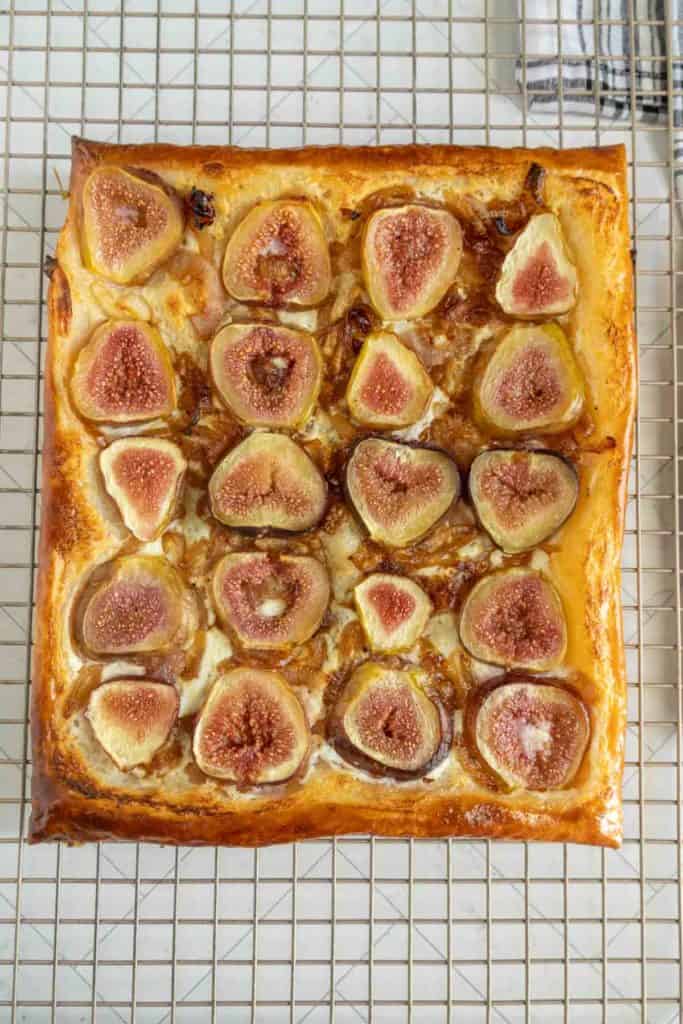 A rectangular pastry topped with sliced figs is cooling on a wire rack.