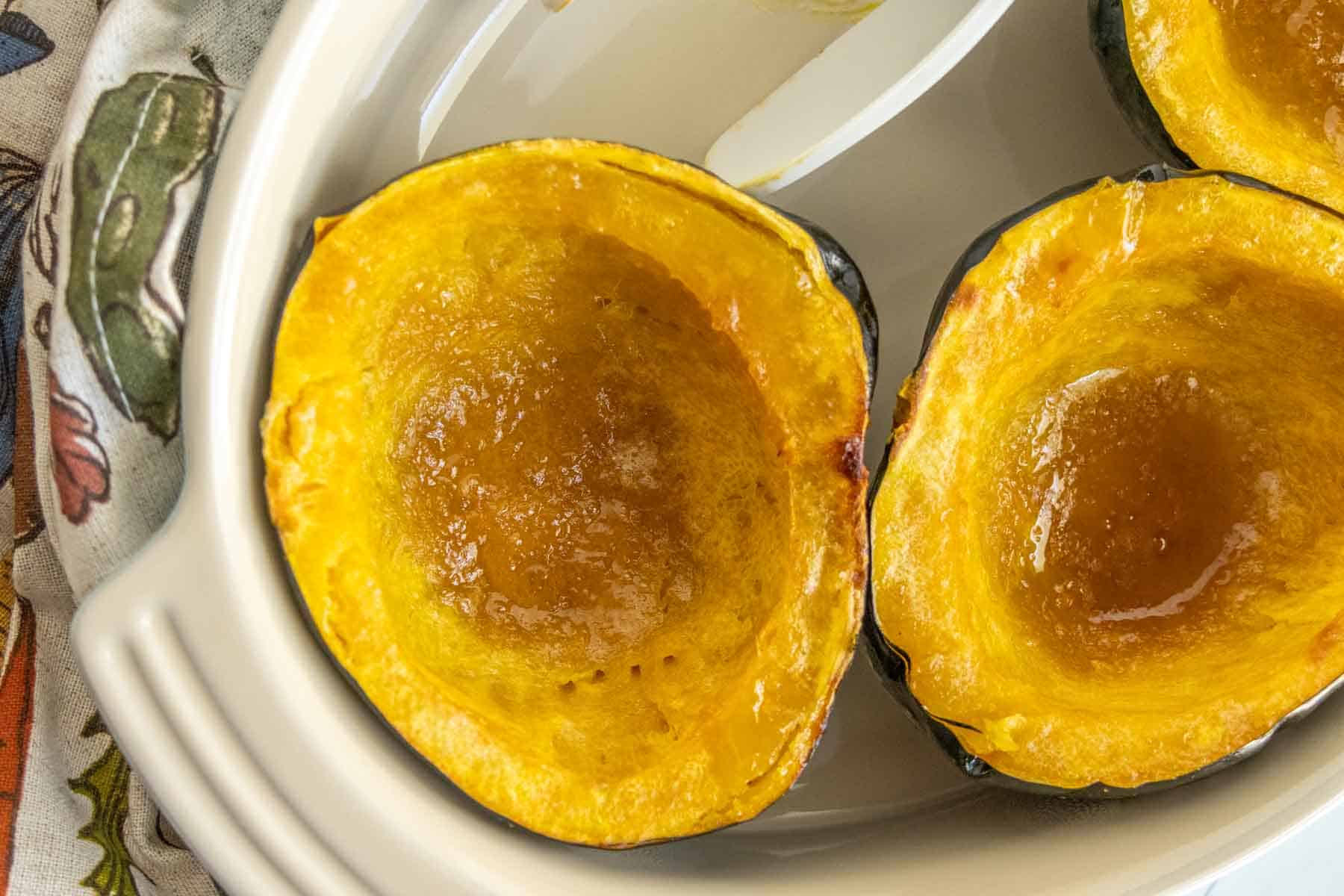 A close-up of roasted acorn squash halves in a white dish, showcasing the golden-brown, caramelized interior.