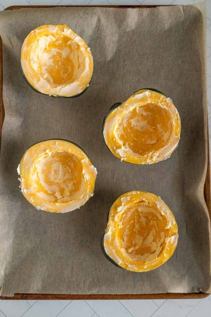 Four acorn squash halves with seeds removed, placed face-up on a parchment-lined baking sheet.