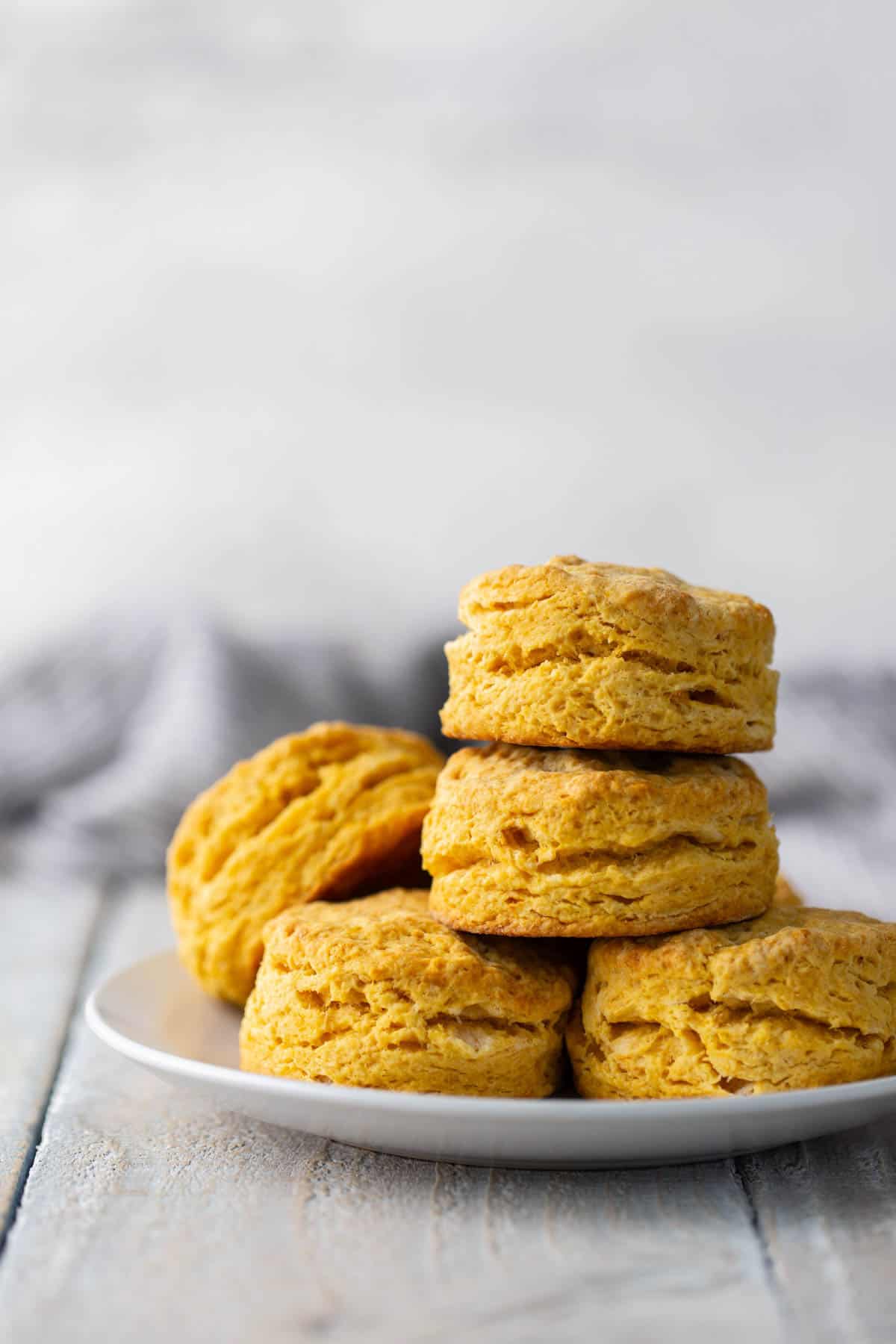 A plate with a stack of five golden-brown biscuits on a light wooden surface, with a blurred background.