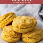 A plate of sweet potato biscuits is stacked on a wooden surface with a gray cloth in the background. The image includes text that reads, "sweet potato biscuits: tender and flaky.