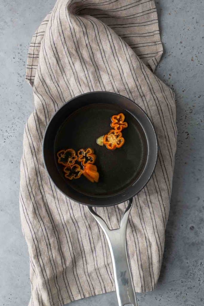 A small frying pan with slices of orange and brown bell peppers sits on a striped cloth.