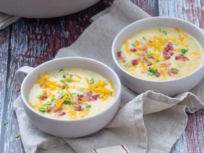 baked potato soup in two shallow bowls with dutch oven behind