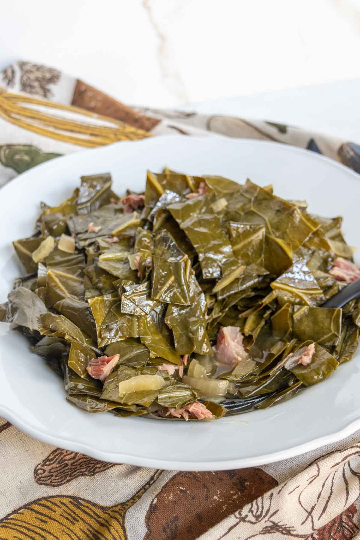 A plate of cooked collard greens mixed with pieces of ham on a white dish.