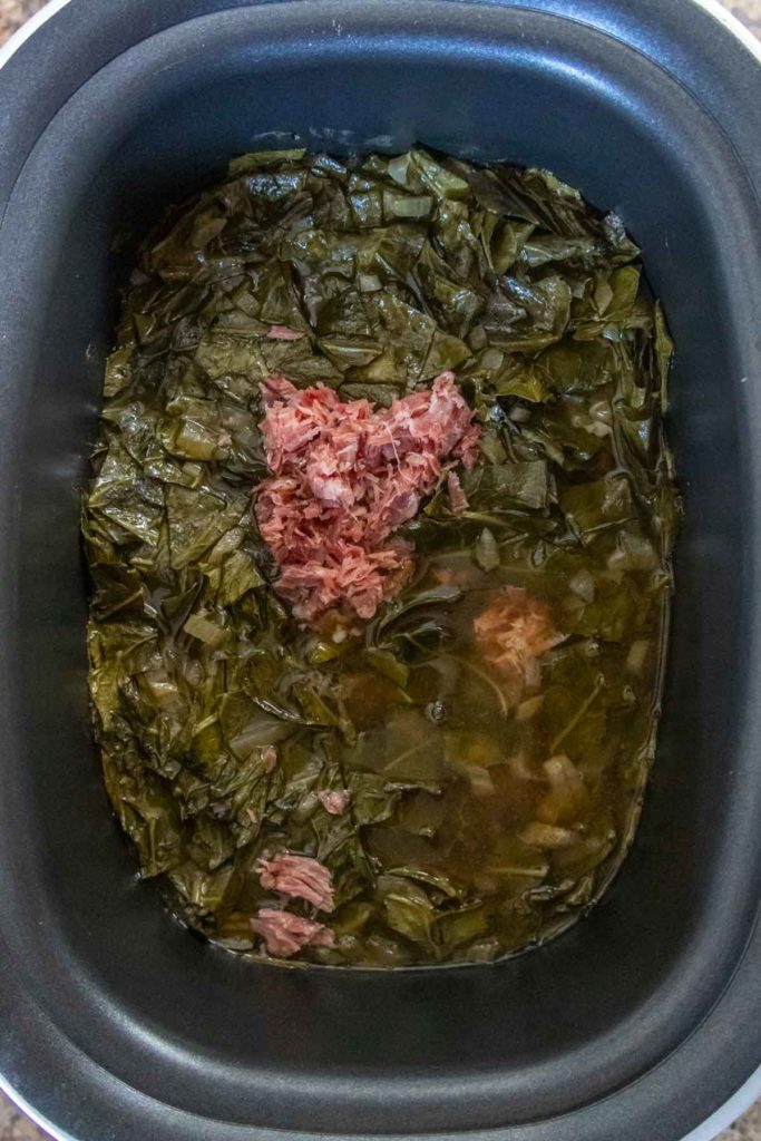 Slow cooker with cooked collard greens and shredded meat.