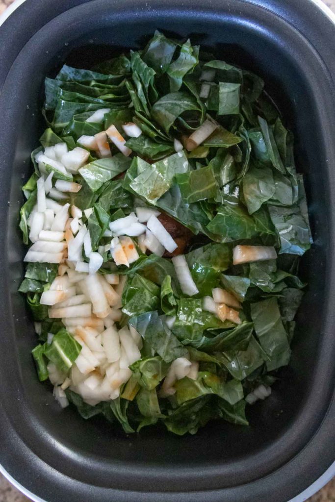 Chopped collard greens and diced onions in a slow cooker.