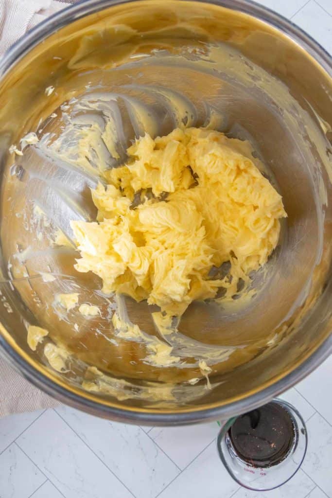 Buttercream mixture in a metal mixing bowl with a beater visible at the bottom.