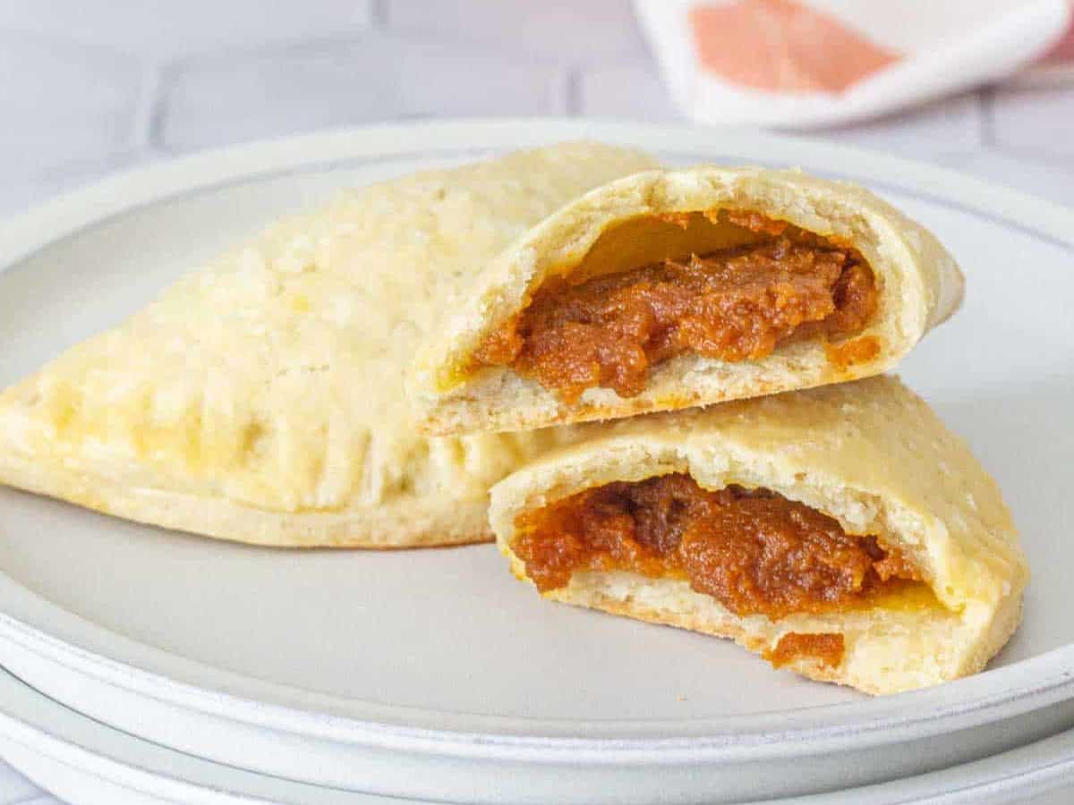 Pumpkin empanadas on a plate with one broken in half to see filling.