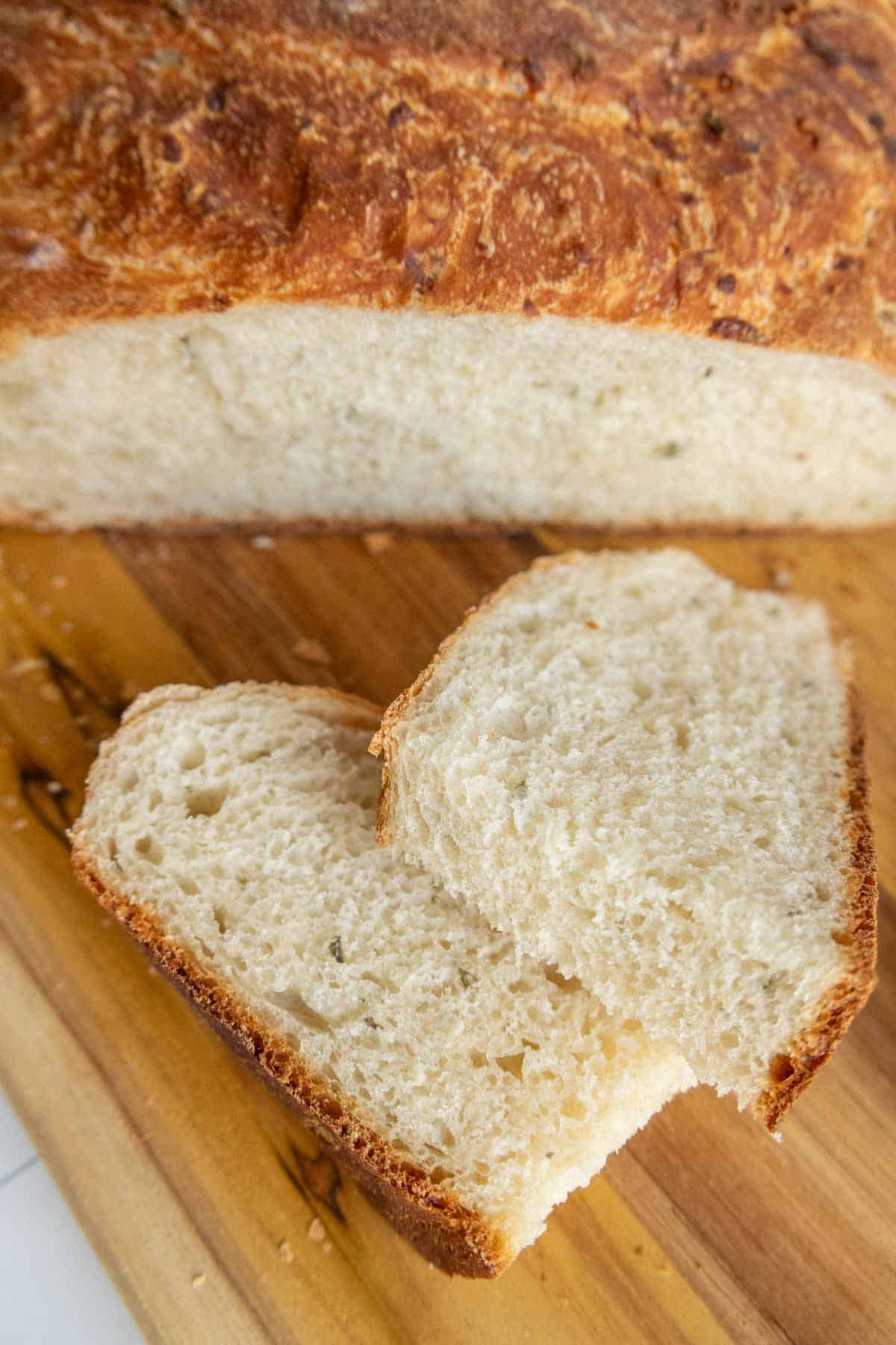 Two slices of homemade bread lie on a wooden cutting board, with a larger loaf in the background.