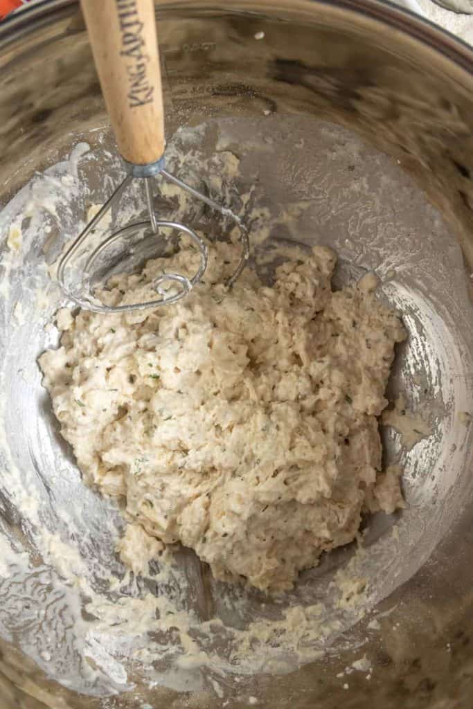 A mixing bowl containing rough, wet dough with a wire dough whisk resting on the side.