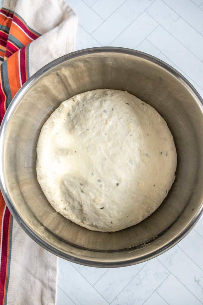 A bowl of risen dough on a light-colored countertop, with a striped cloth partially visible next to it.