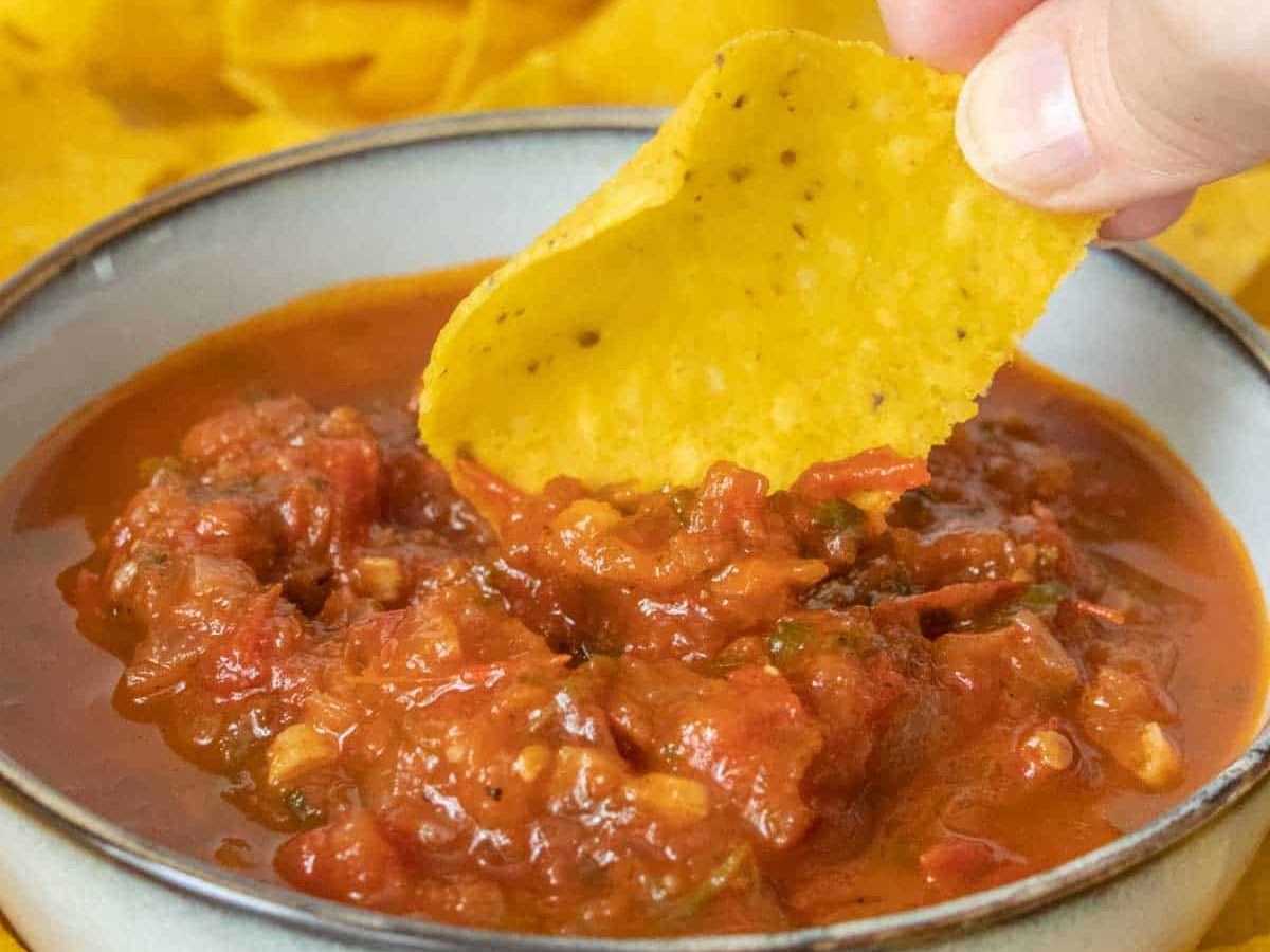 A hand dipping a tortilla chip into a bowl of salsa.