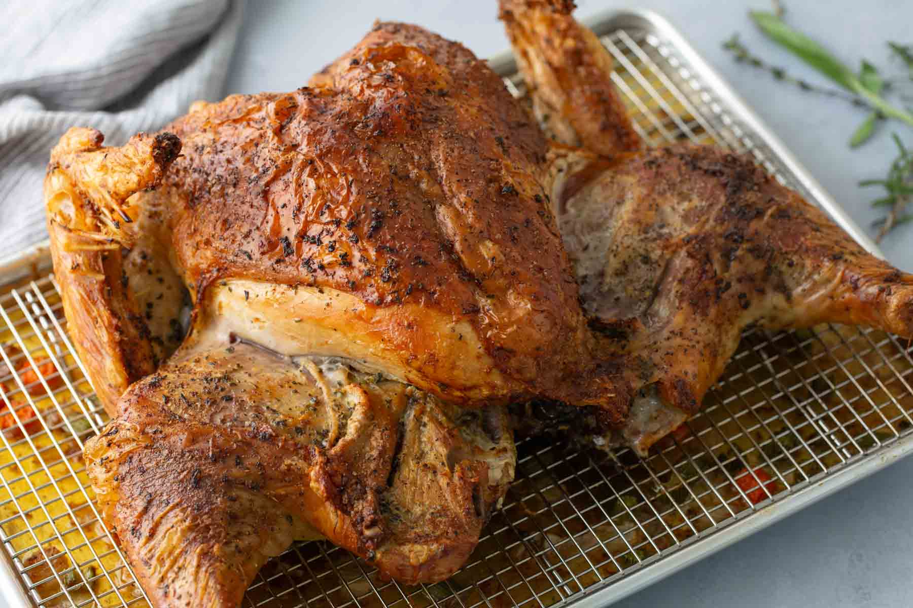 Roasted spatchcocked chicken on a cooling rack over a baking sheet, seasoned with herbs and spices.