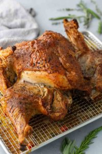 Roasted chicken on a cooling rack with crispy, golden skin, garnished with fresh herbs, placed on a light-colored surface.