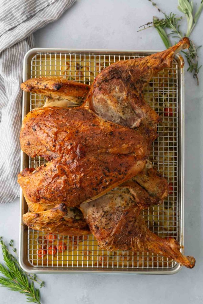 Roasted spatchcocked turkey on a wire rack over a baking sheet, garnished with rosemary sprigs.