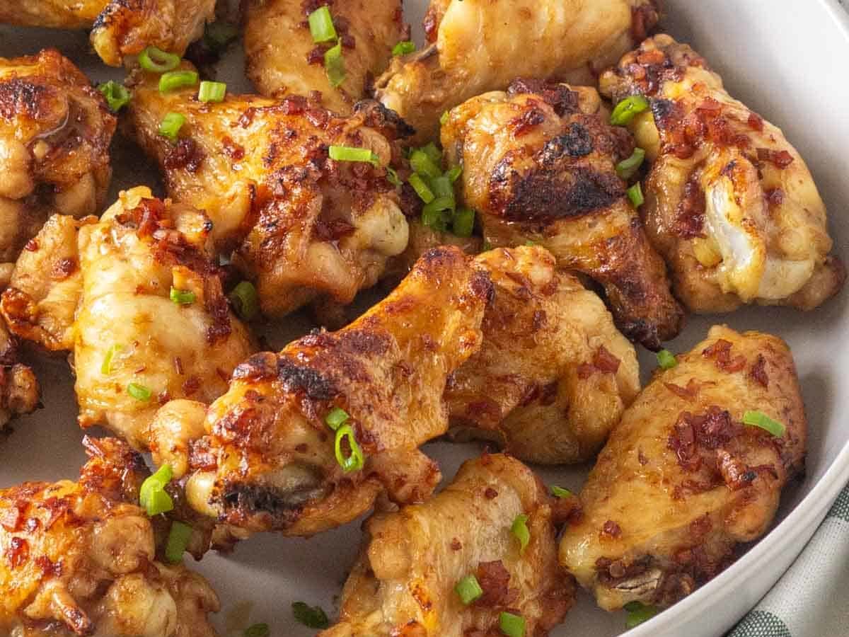 A bowl of roasted chicken wings garnished with green onions.