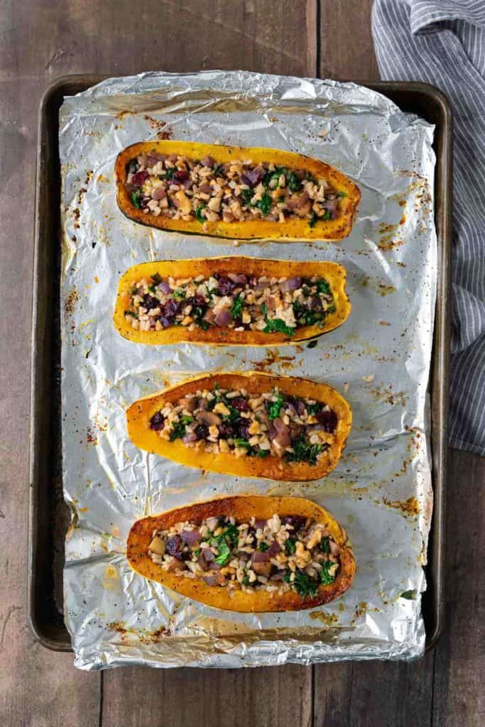 Four stuffed squash halves on a foil-lined baking sheet, filled with rice, vegetables, and herbs.