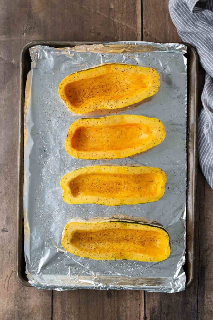 Four halved acorn squashes seasoned and placed on a foil-lined baking sheet.