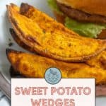 Close-up of sweet potato wedges and a burger on a plate. Text overlay reads "Sweet Potato Wedges Easy Side Dish. Get the recipe at stetted.com".