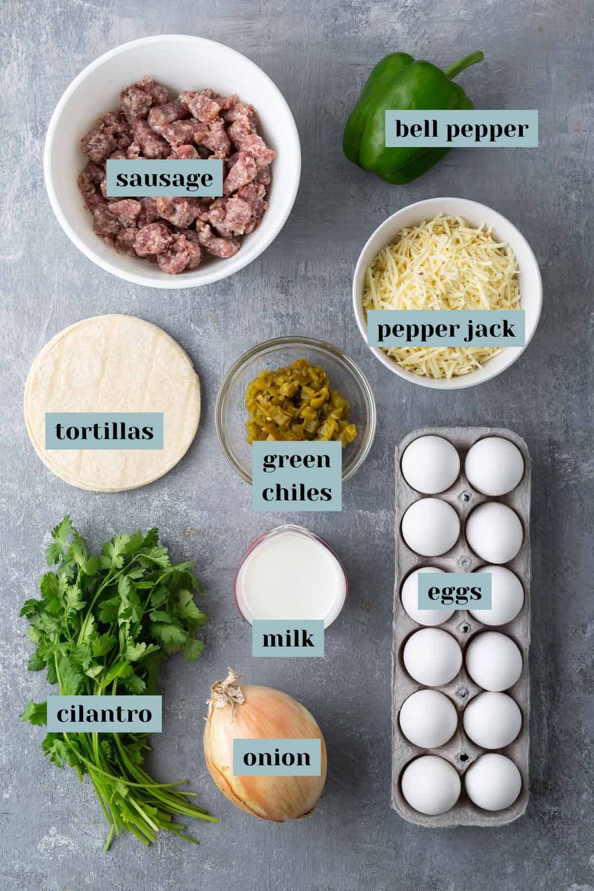 Ingredients laid out on a surface: sausage, bell pepper, tortillas, pepper jack cheese, green chiles, eggs, milk, onion, and cilantro.