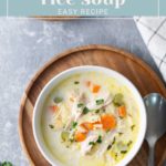 Bowl of turkey rice soup with vegetables on a wooden tray, spoon on the side.