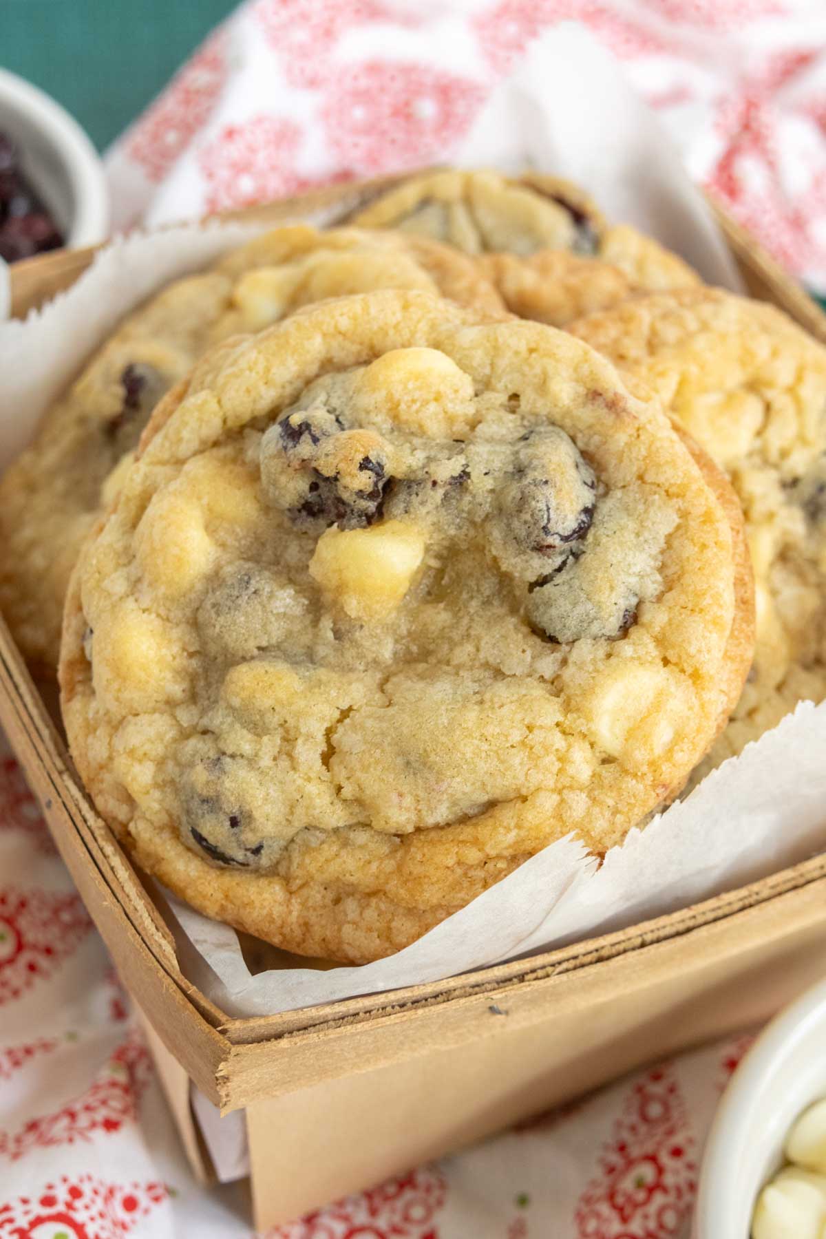 A box filled with white chocolate chip cookies on a red and white patterned cloth.