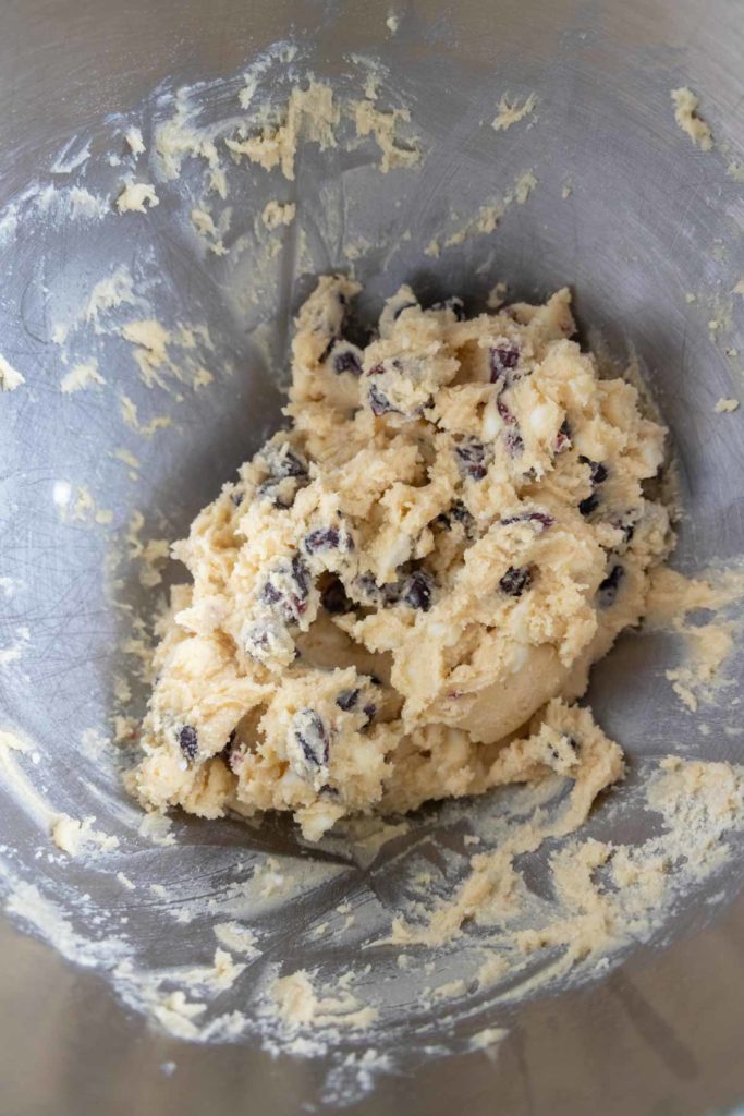 Close-up of cookie dough with chocolate chips and raisins in a mixing bowl.