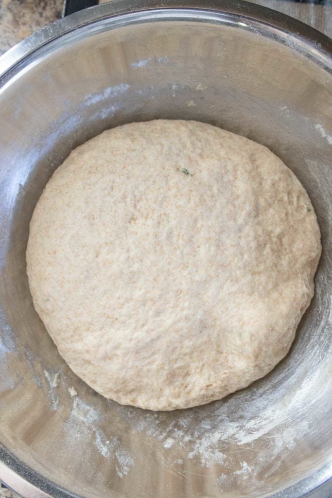 A ball of bread dough rests in a metal mixing bowl.