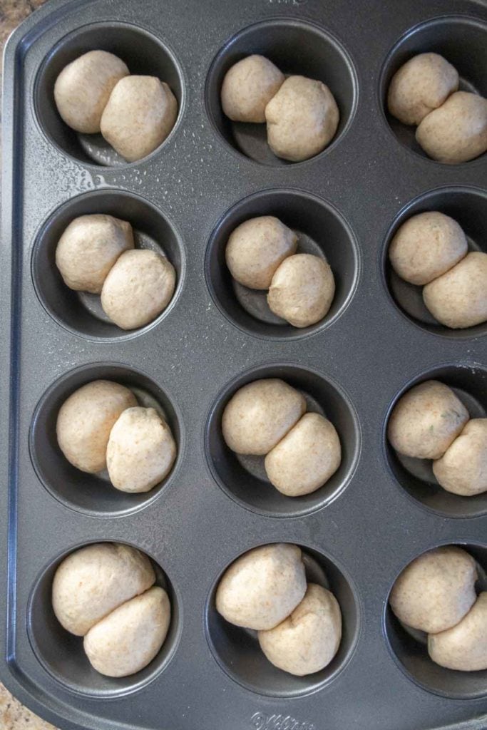 A muffin tin with compartments filled with raw dough balls, ready for baking.