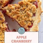 Close-up of a sliced apple cranberry pie with a crumb topping. A text overlay reads, "Apple Cranberry Pie. Get the recipe at stetted.com.