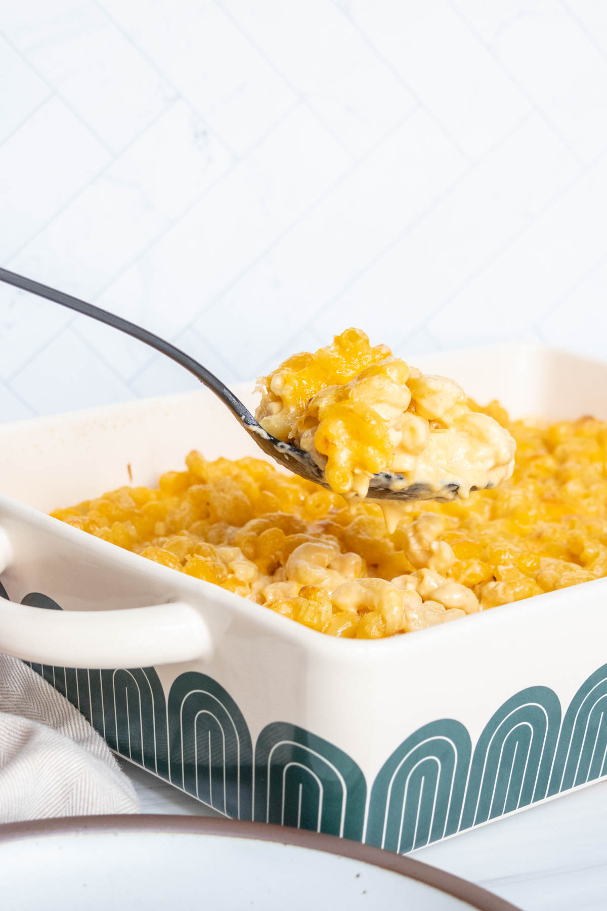 A spoon scoops a portion of baked macaroni and cheese from a casserole dish.